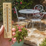 une personne dans son jardin regarde la température grimper sur un thermomètre